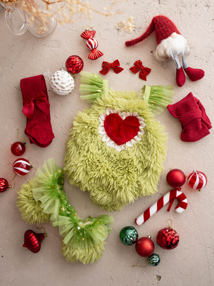 Little Grump green faux-fur romper with a red fur heart and matching leg warmers, styled with red Christmas baubles and a candy cane - Before & Ever Kids