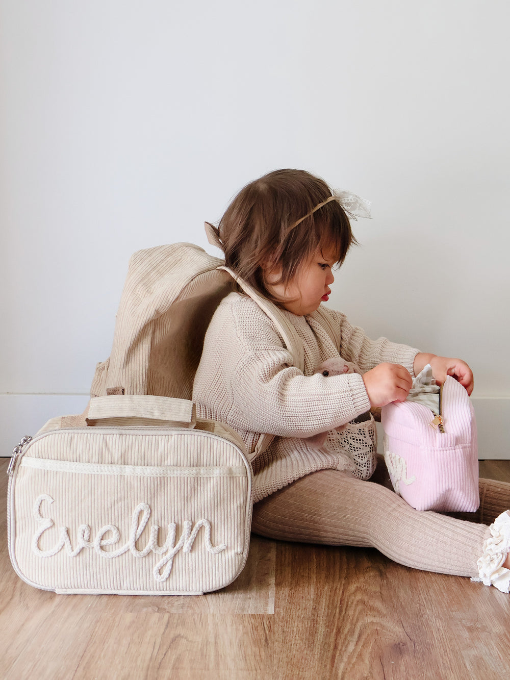 Beige corduroy lunch bag embroidered Evelyn beside a toddler wearing the matching backpack