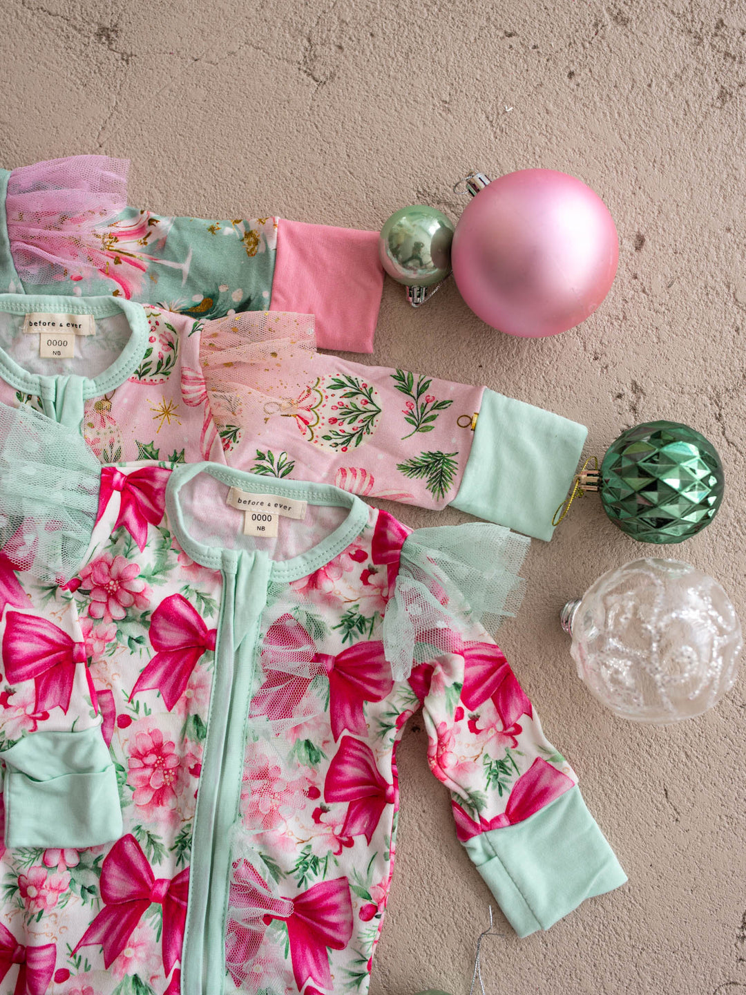 All I Wish Christmas baby onesies and topknots laid out together including the Pink Bow print - Before & Ever Kids
