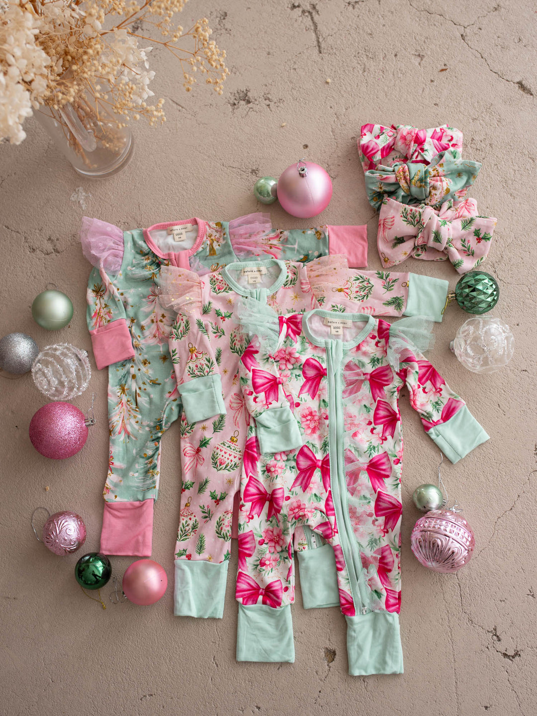 All I Wish Christmas baby onesies and topknots laid out together including the Pink Bow print - Before & Ever Kids