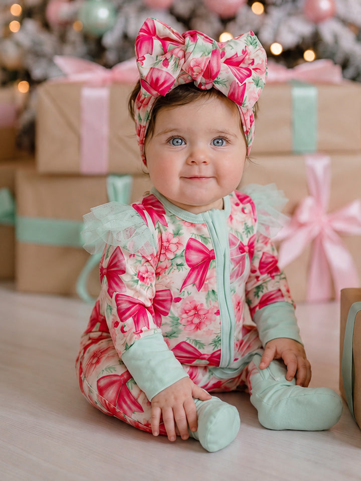 All I Wish Pink Bow baby onesie worn by a seated baby girl in the matching topknot headwrap, showing the mint cuffs and footed legs - Before & Ever Kids