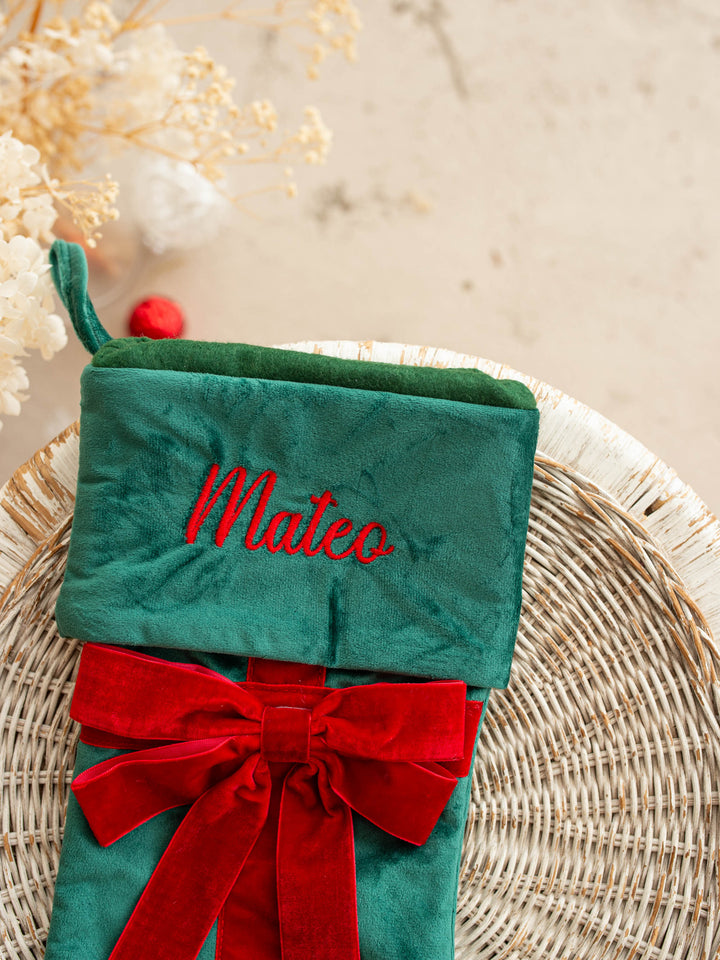 All Wrapped Up personalised Christmas stocking, close up of the green stocking's embroidered name and red velvet bow - Before & Ever Kids