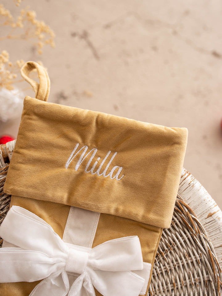 All Wrapped Up personalised Christmas stocking, close up of the gold stocking's embroidered name and white bow - Before & Ever Kids