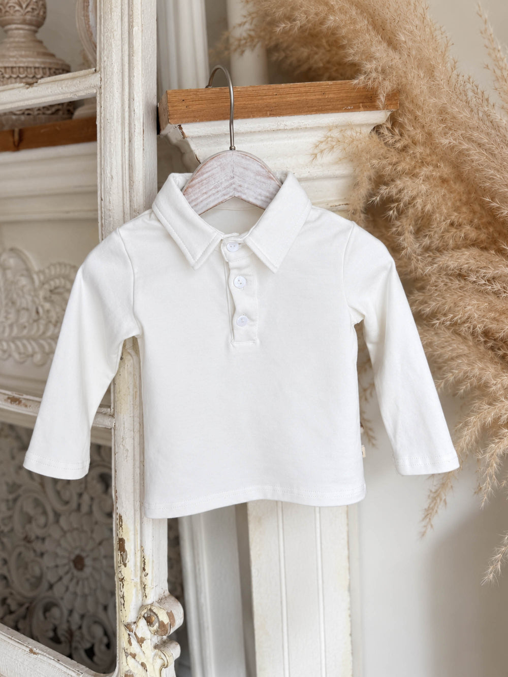 Everyday Cotton Polo, white long sleeve cotton polo, hanging on a hanger beside dried pampas - Before & Ever Kids