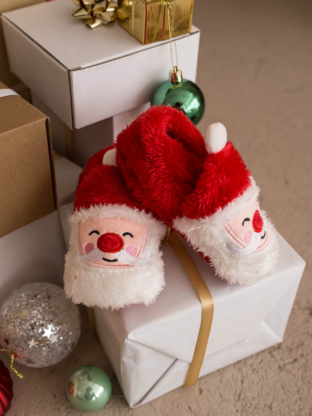 Santa Baby Slippers red fluffy Santa slippers resting on a wrapped present - Before & Ever Kids