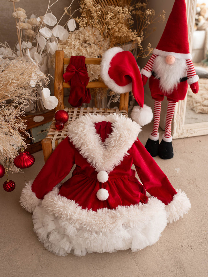 She Came to Sleigh red velvet Santa dress on a wooden chair with a Santa hat beside it - Before & Ever Kids