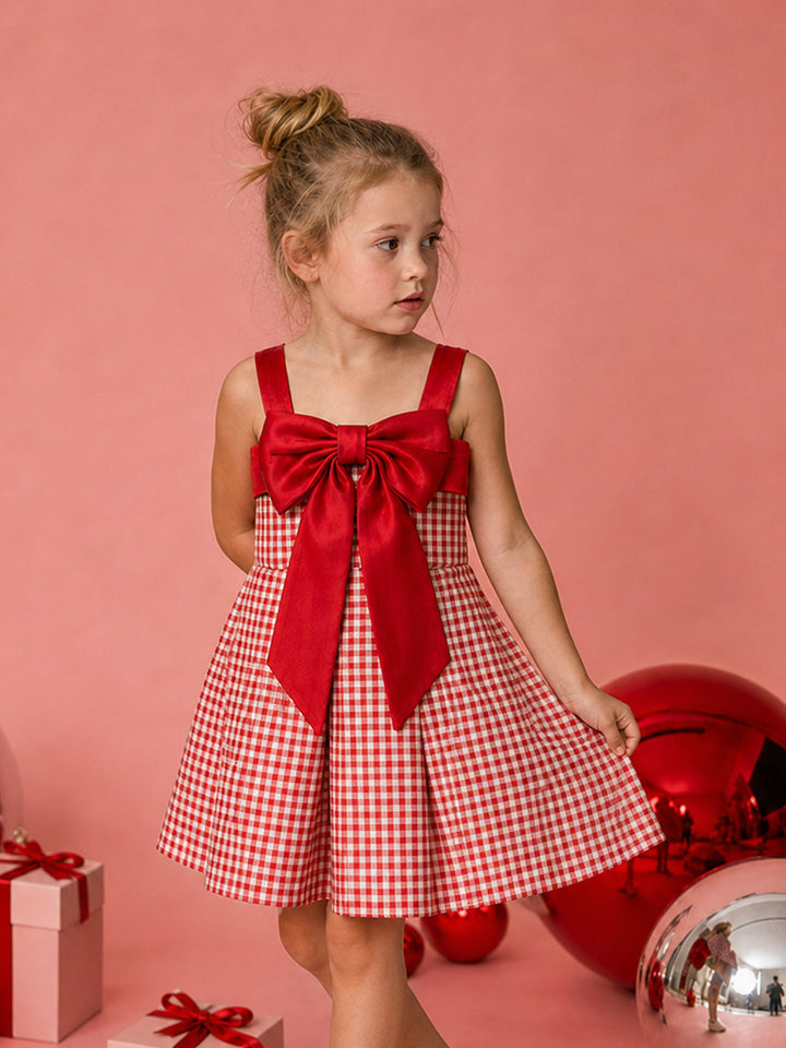 Sweet as Pie red and white gingham Christmas dress with a red satin bow, holding out the pleated skirt beside red baubles