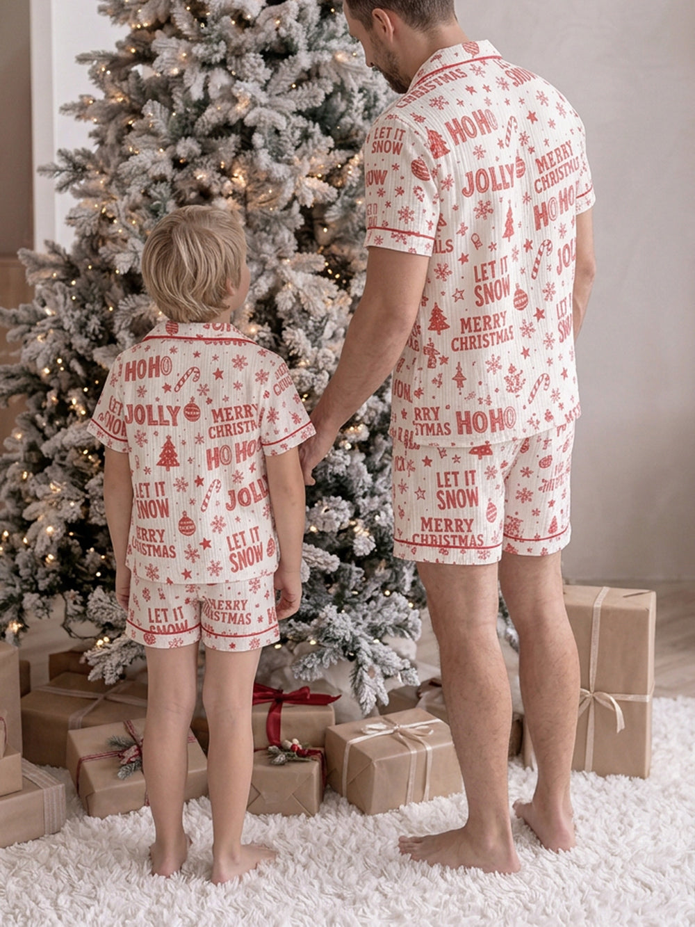 Twas the Night family Christmas pyjamas, white cotton muslin with a red Christmas print, dad and the boy standing by the tree in short sleeves and shorts, back view - Before & Ever Kids