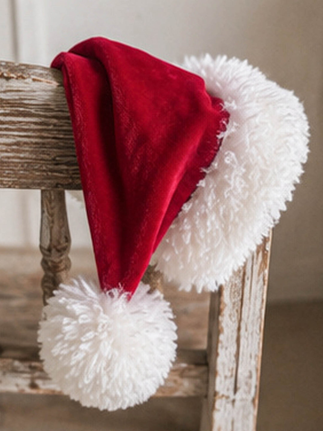 Velvet Santa Hat in deep red, hanging over the back of a wooden chair - Before & Ever Kids