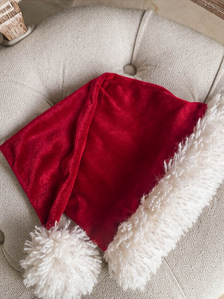 Velvet Santa Hat in deep red, resting on a cream armchair - Before & Ever Kids