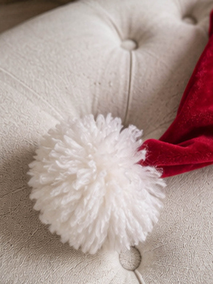 Velvet Santa Hat in deep red, close up of the pom-pom resting on a cream armchair - Before & Ever Kids